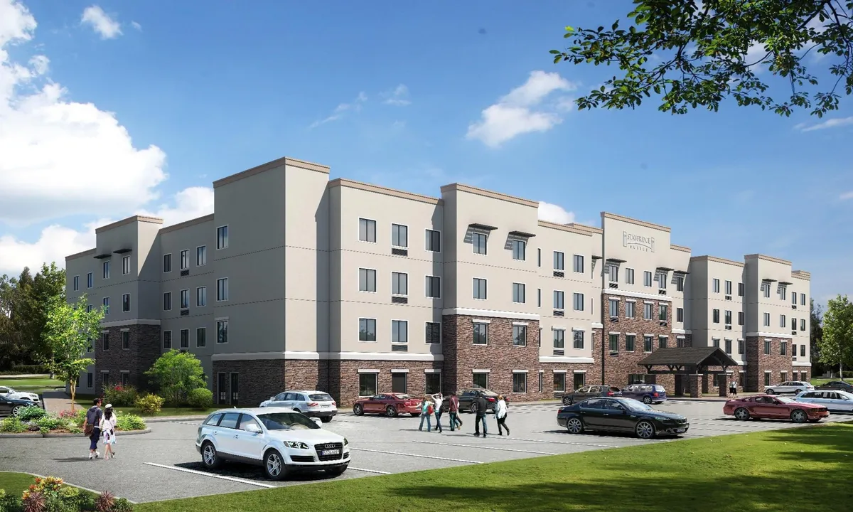 This image captures the exterior of the hotel, showcasing the building facade, entrance awning, landscaped area, and convenient parking lot. The scene feels friendly and welcoming, suggesting ease of arrival and proximity to local attractions.