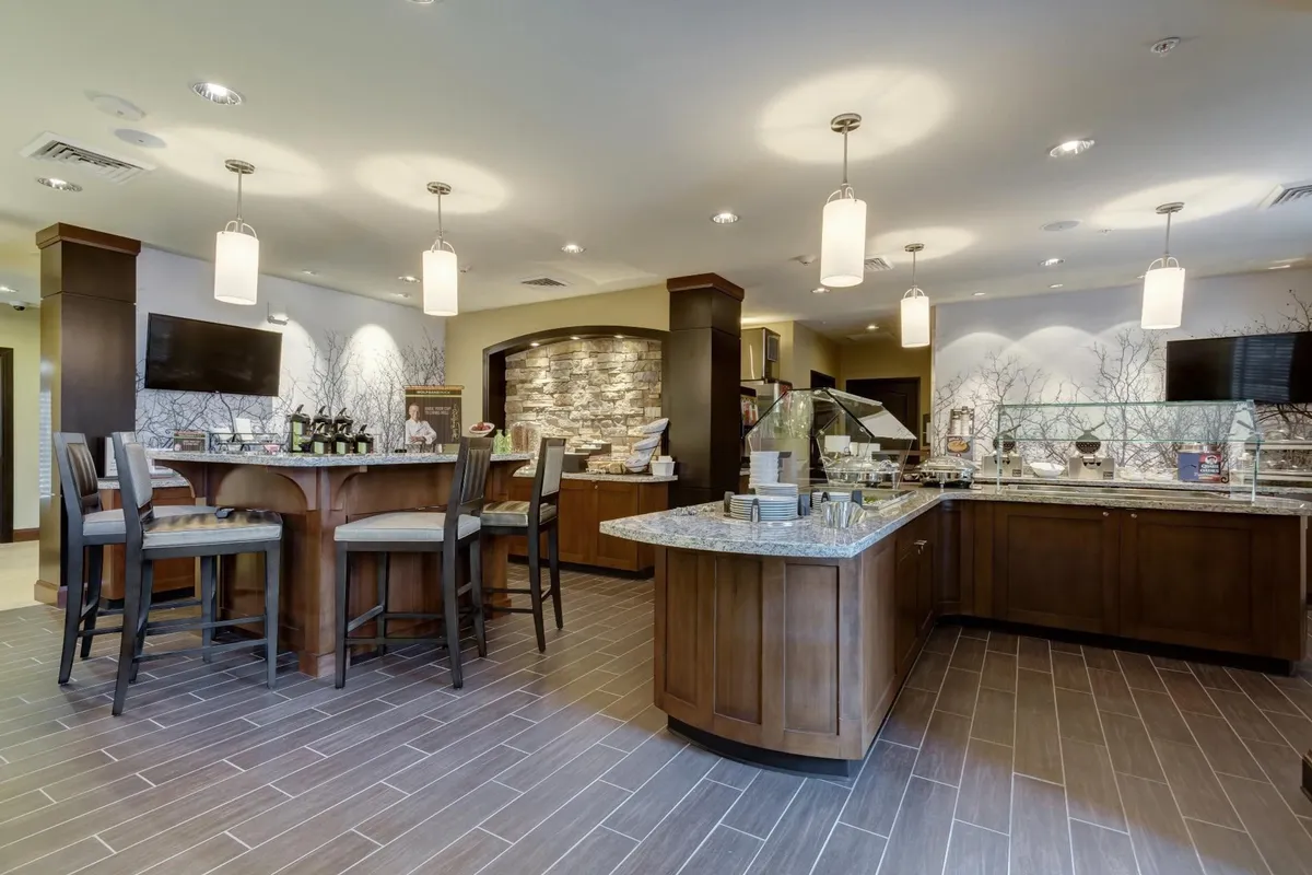 This image features a central serving area surrounded by bar seating and a striking stone feature wall. The inviting setup suggests a space designed for dining and casual gatherings, with ample room for guests to enjoy meals together. The bar area hints at convenient access to food and beverages, reflecting the communal dining experience described in the section.