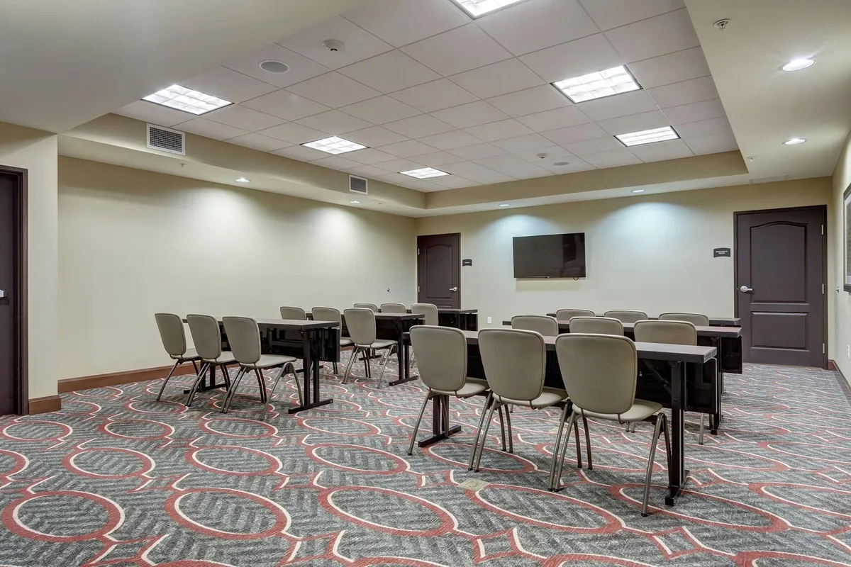 An organized interior meeting space with rectangular tables, stacked chairs, a television screen, and a stylish carpet. The setup is business-like and ready for successful meetings, training programs, or networking events.